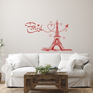 May include: Red Eiffel Tower wall decal with the word "Paris" and hearts. The decal is on a white wall above a white couch with a wooden coffee table.