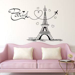 May include: Black and white illustration of the Eiffel Tower with a heart and airplane design. The text "Paris" is written in a cursive font. The illustration is on a white wall above a pink sofa.