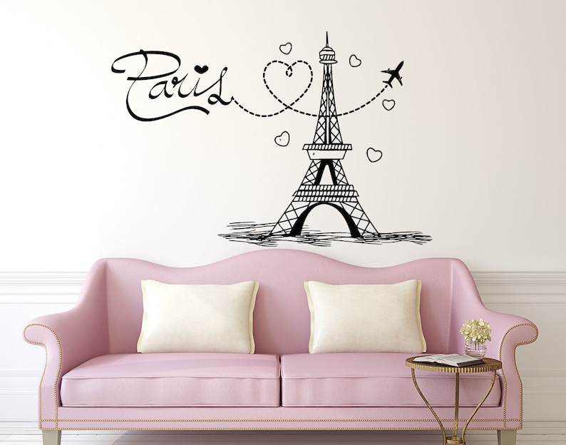 May include: Black and white illustration of the Eiffel Tower with a heart and airplane design. The text "Paris" is written in a cursive font. The illustration is on a white wall above a pink sofa.