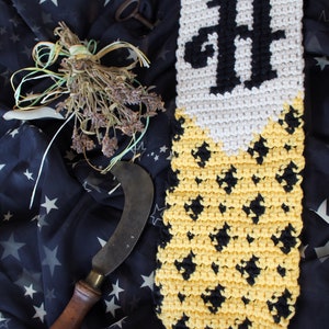 May include: A crocheted wall hanging with a black "H" and a yellow and black diamond pattern. The hanging is made with white, yellow, and black yarn.