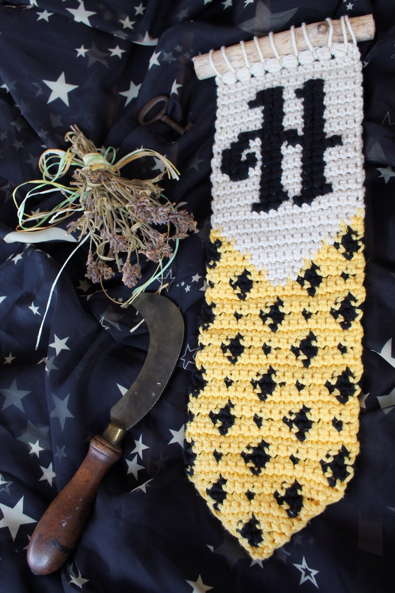 May include: A crocheted wall hanging with a black "H" and a yellow and black diamond pattern. The hanging is made with white, yellow, and black yarn.