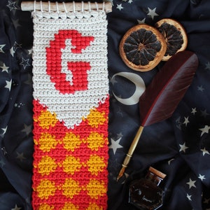 May include: A crocheted tapestry with a red "G" and a red and yellow checkered pattern. The tapestry is hanging on a black fabric background with stars.