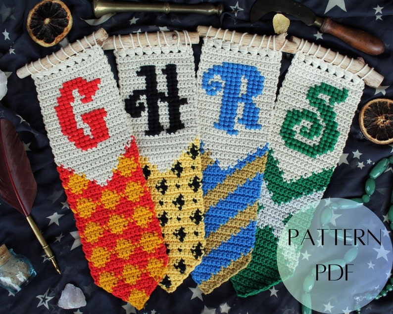 May include: Four crocheted banners with the Hogwarts house crests and initials: Gryffindor, Hufflepuff, Ravenclaw, and Slytherin. The banners are white with colored details and are hanging from wooden dowels. The text "PATTERN PDF" is visible in the bottom right corner.