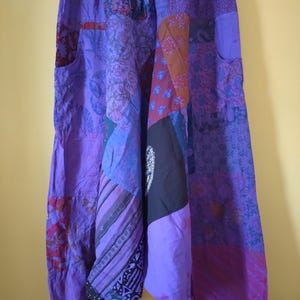 Puede incluir: Pantalones holgados con un diseño de patchwork en varios tonos de morado, violeta y magenta. La prenda incluye una cintura elástica con cordón, bolsillos laterales y puños fruncidos en los tobillos con diversos estampados florales.