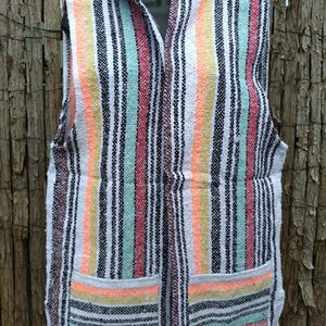 May include: A sleeveless, hooded vest with a colorful striped pattern. The vest features vertical stripes in white, black, orange, yellow, red, and teal. It has two front pockets and a zipper closure. The vest is displayed on a black mannequin.