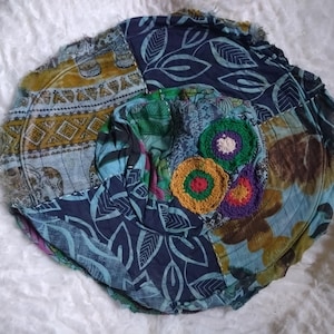 Peut inclure: Un chapeau patchwork avec divers tissus à motifs bleus, verts, jaunes et bruns. Le chapeau présente plusieurs appliqués de fleurs crochetées de différentes couleurs, ajoutant une touche unique et faite à la main.