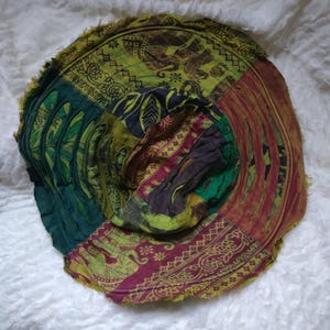 May include: A patchwork hat with a wide brim, featuring patterned fabrics in green, burgundy, and gold. The hat has a frayed edge and a round crown, with floral and elephant motifs. The hat's diameter is approximately 30 cm.