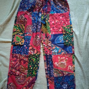 May include: Patchwork trousers in a vibrant mix of colours and patterns. The trousers feature a patchwork design with various fabric squares in shades of blue, red, green, and purple. They have an elasticated waistband and a relaxed fit.