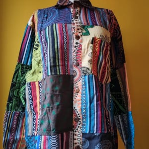 May include: A patchwork shirt with a button-down design, showcasing a mix of vibrant patterns and textures. It has a collar, long sleeves, and wooden buttons. The design incorporates stripes, floral, and geometric motifs.