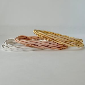 May include: Three coiled metal bracelets in silver, rose gold, and gold.