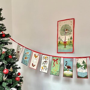 May include: A Christmas advent calendar banner with a red and white string and 10 colourful cards with numbers and illustrations. The cards feature a variety of winter themes, including birds, geese, and a Christmas tree.