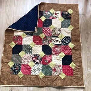 Può includere: Una trapunta patchwork con uno sfondo marrone e una varietà di quadrati colorati. La trapunta è composta da diversi tessuti con motivi floreali, paisley e geometrici. La trapunta è bordata da un bordo marrone e da un bordo giallo.