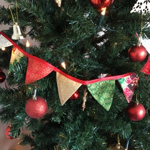 May include: A red, green, and gold Christmas bunting with a red ribbon, hanging on a Christmas tree decorated with red ornaments and lights.