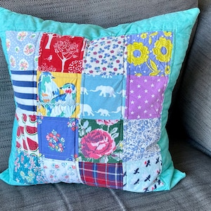 Può includere: Un cuscino turchese con un design a patchwork che presenta vari tessuti colorati con motivi floreali, animali e geometrici.