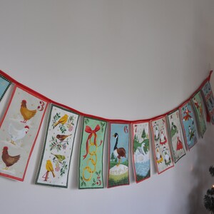 May include: A Christmas advent calendar banner with red and white string and 12 flags. Each flag has a different number, animal, and design. The flags are in a curved shape.