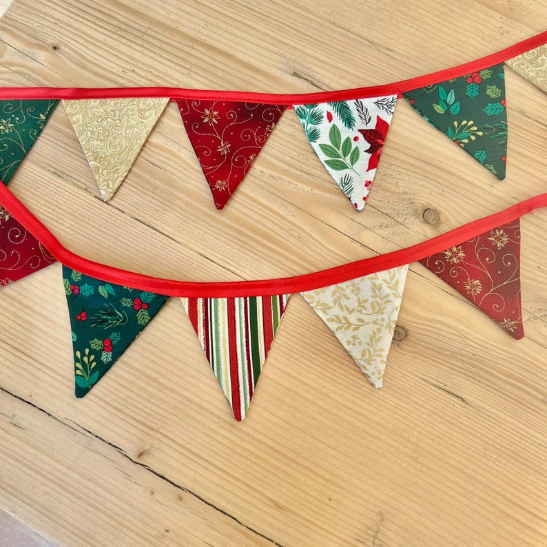 May include: A festive Christmas banner with alternating red, green, and gold fabric triangles. Each triangle features a different holiday-themed pattern, including snowflakes, holly, and pine branches.