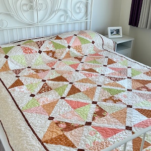 May include: A white metal bed frame with a decorative headboard and a patchwork quilt in shades of brown, pink, and green.