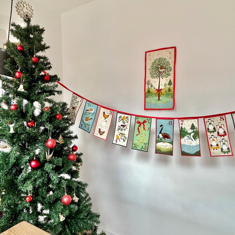 May include: A Christmas advent calendar banner with a red and white string and 10 colorful cards with numbers and illustrations. The cards feature a variety of winter themes, including birds, geese, and a Christmas tree.