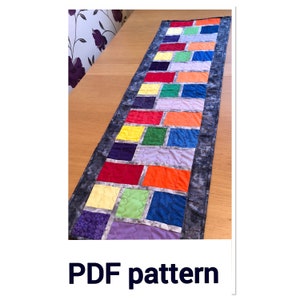 May include: A colorful table runner with a rainbow pattern of squares. The runner is made of fabric and has a gray background with a subtle pattern.  PDF pattern.