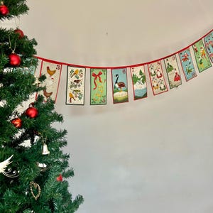 May include: A red and white Christmas garland with numbered flags featuring illustrations of birds, animals, and people. The garland is hanging from a white wall.