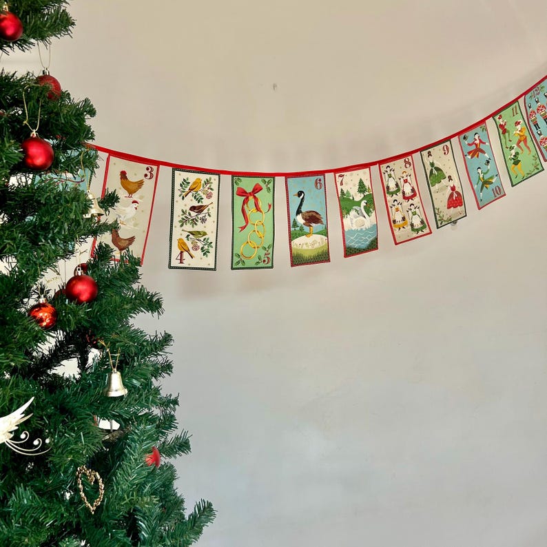 May include: A red and white Christmas garland with numbered flags featuring illustrations of birds, animals, and people. The garland is hanging from a white wall.