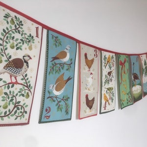 May include: A Christmas advent calendar banner with 10 colorful fabric panels featuring different birds, animals, and holiday motifs. Each panel has a number, from 1 to 10, and is connected by a red ribbon.