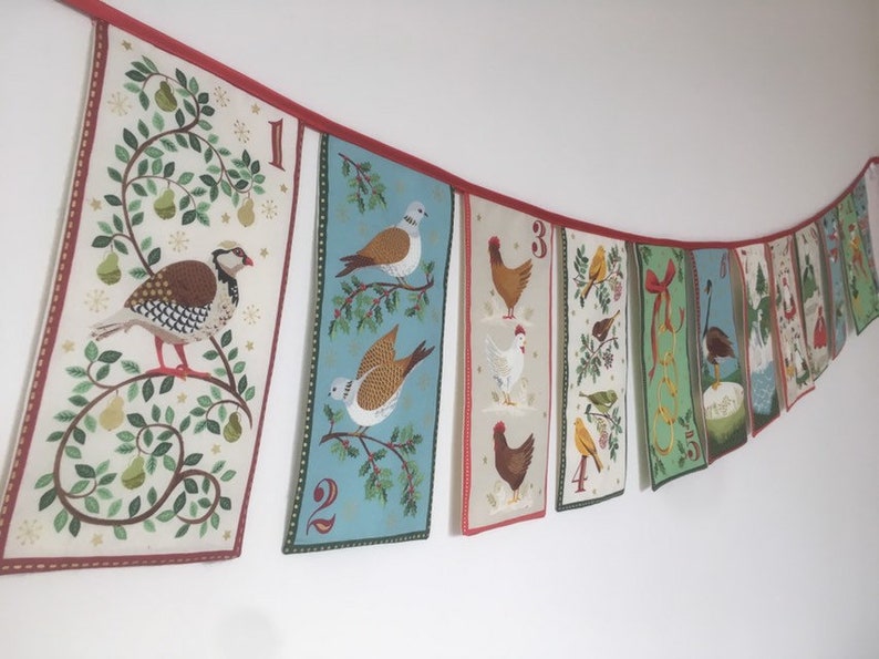 May include: A Christmas advent calendar banner with 10 colorful fabric panels featuring different birds, animals, and holiday motifs. Each panel has a number, from 1 to 10, and is connected by a red ribbon.