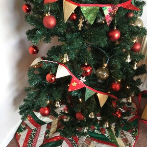 May include: A Christmas tree decorated with red and gold ornaments, a red and gold fabric garland, and a red and green patchwork tree skirt.
