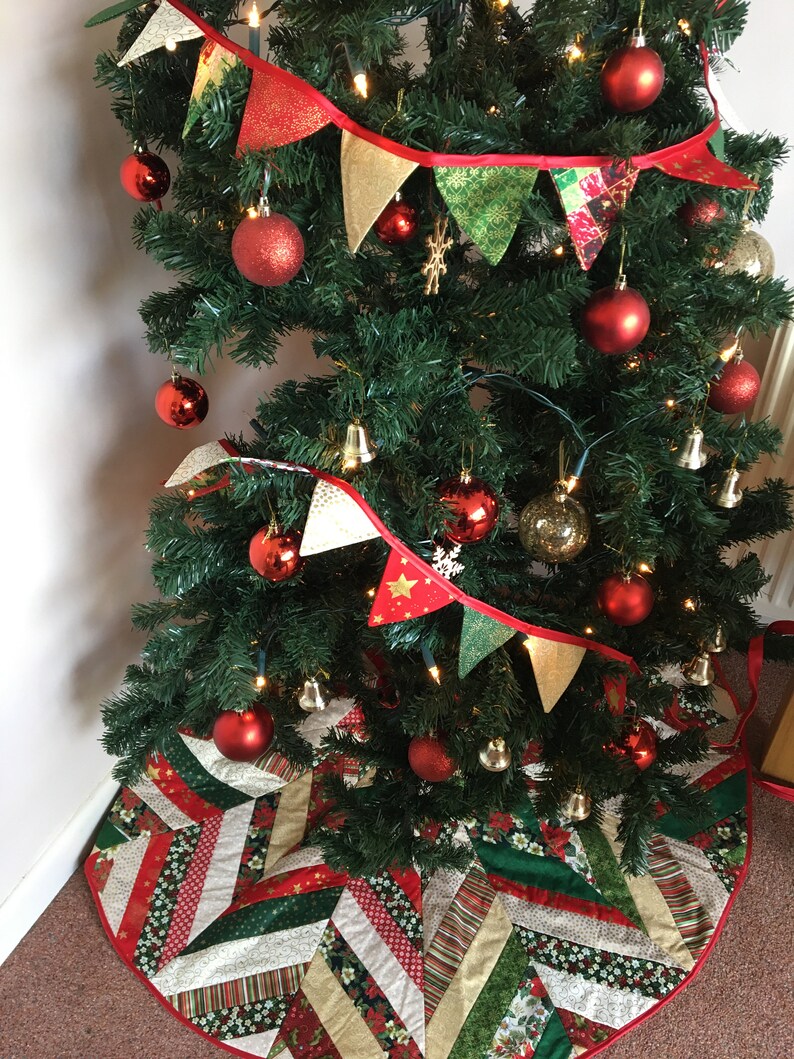 May include: A Christmas tree decorated with red and gold ornaments, a red and gold fabric garland, and a red and green patchwork tree skirt.