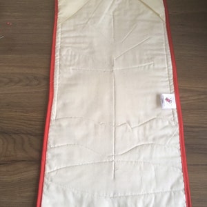 May include: A white quilted placemat with a red border. The placemat has a quilted design of a tree branch with leaves.
