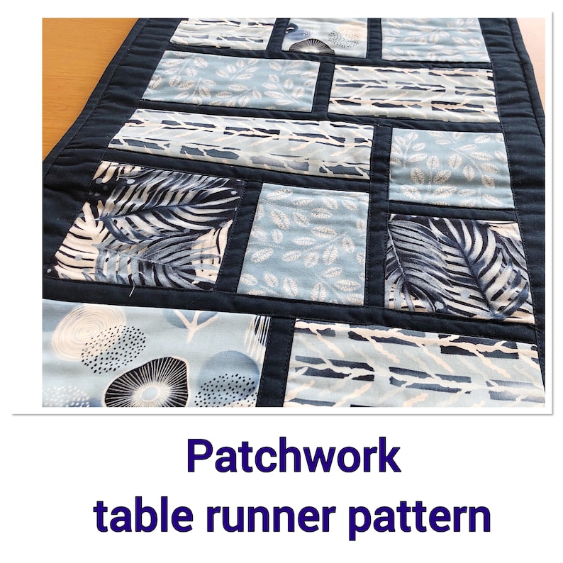 May include: A patchwork table runner pattern with a navy blue background and blue and white fabric squares. The fabric squares feature different patterns, including leaves, dots, and stripes.