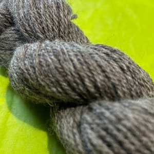 Puede incluir: Un ovillo de hilo gris oscuro con una textura peluda.