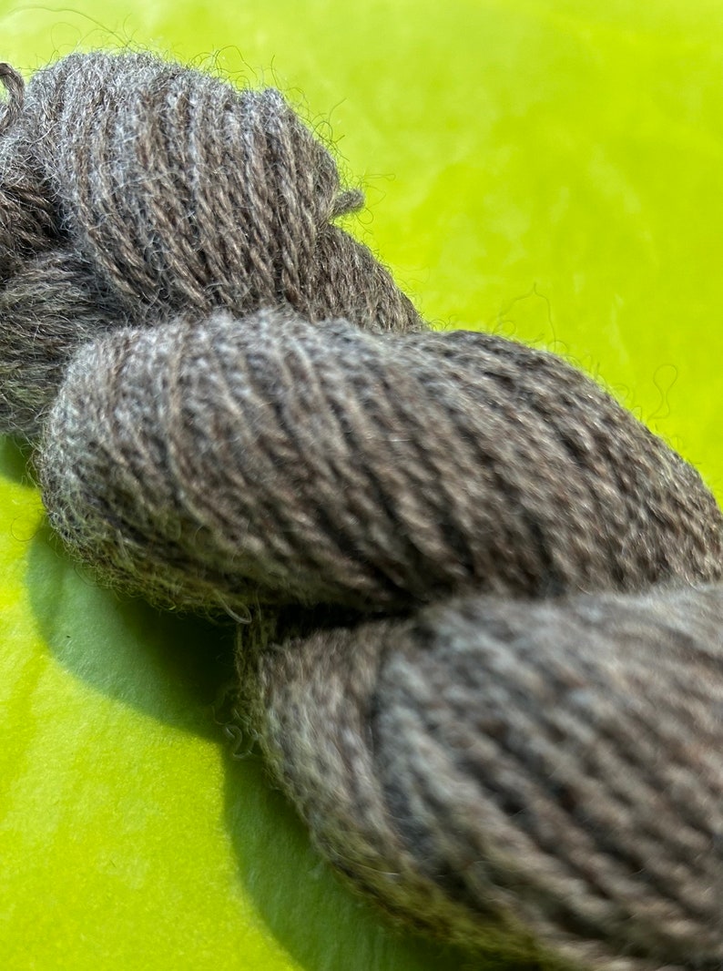 Puede incluir: Un ovillo de hilo gris oscuro con una textura peluda.