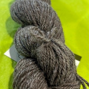 Puede incluir: Un ovillo de lana gris oscuro con una textura peluda. La lana est&aacute; enrollada en forma de bola y est&aacute; lista para tejer o hacer ganchillo.