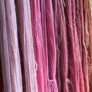 K&ouml;nnte beinhalten: Nahaufnahme von verschiedenfarbigen rosa Garnen, die vertikal h&auml;ngen. Die Farben reichen von hellrosa bis zu tiefem Ros&eacute; und erzeugen einen Farbverlauf. Die Textur des Garns ist sichtbar, was auf eine weiche, nat&uuml;rliche Faser hindeutet. Ideal f&uuml;r Strick- und H&auml;kelprojekte.