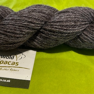 Puede incluir: Una madeja de hilo de alpaca gris oscuro. El hilo est&aacute; hecho por Cotswold Alpacas, que cr&iacute;an mejores colores. La etiqueta dice "Cotswold Alpacas, Breeders Better Colors, www.cotswoldalpacas.co.uk."