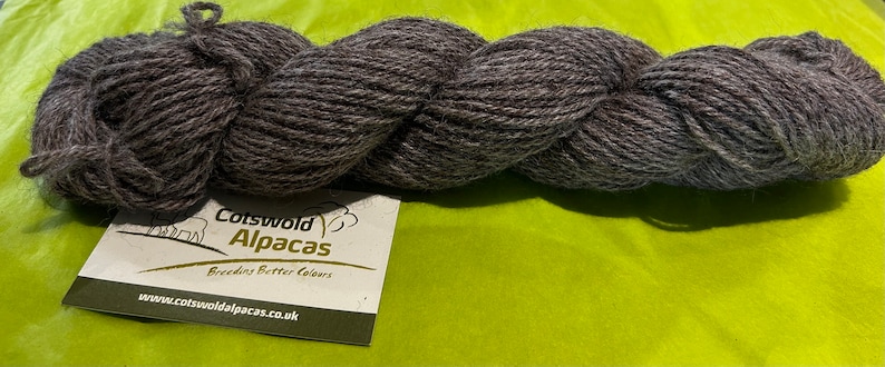 Puede incluir: Una madeja de hilo de alpaca gris oscuro. El hilo est&aacute; hecho por Cotswold Alpacas, que cr&iacute;an mejores colores. La etiqueta dice "Cotswold Alpacas, Breeders Better Colors, www.cotswoldalpacas.co.uk."