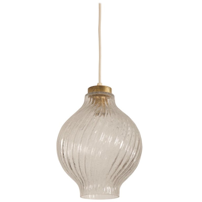 May include: Clear glass pendant light with a textured, swirled design. The light fixture has a bulbous shape and a brass-colored metal cap. A white cord suspends the light from above, creating a vintage aesthetic.