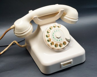 May include: A white rotary dial phone with a green dial and a brown cord. The phone has a simple design and is in good condition.