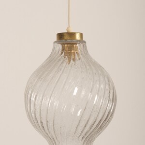 May include: Clear glass pendant light with a textured, swirled design. The light fixture has a brass-colored top and a white cord for hanging. This vintage-style light fixture is suitable for a kitchen or dining room.