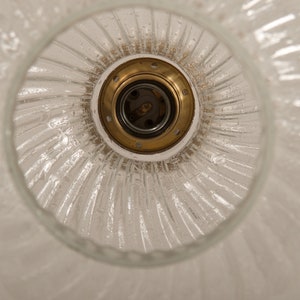 May include: A clear glass light fixture with a textured, swirled design. The fixture has a brass-colored socket and a white base. The light fixture is designed to be mounted on a ceiling.