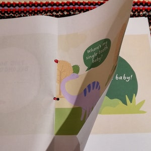 May include: A children's book with a purple dinosaur on the cover. The dinosaur is holding a speech bubble that says "Where's my single-tooth baby?" The book is open to a page with a green background and the text "baby!"