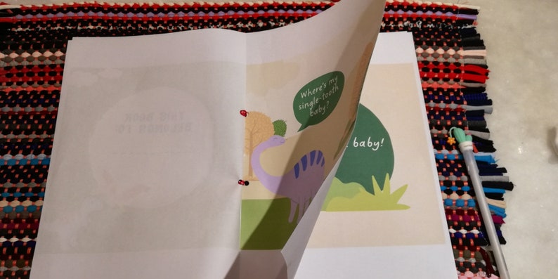 May include: A children's book with a purple dinosaur on the cover. The dinosaur is holding a speech bubble that says "Where's my single-tooth baby?" The book is open to a page with a green background and the text "baby!"