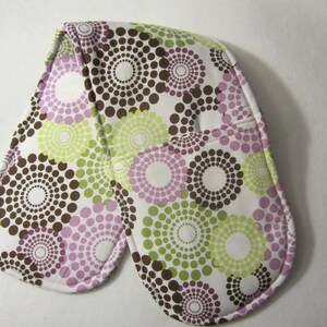 May include: A pair of white oven mitts with a brown, green, and purple circular pattern. The mitts are made of fabric and have a quilted design.