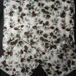 May include: Three white quilted placemats with a pine tree pattern. The placemats are trimmed with a black border.