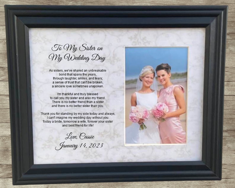 May include: A framed wedding day poem for a sister, with a photo of two women in wedding attire. The poem reads "To My Sister on My Wedding Day" and includes the text "As sisters, we've shared an unbreakable bond that spans the years, through laughter, smiles, and tears; a sense of trust that can't be broken, a sincere love sometimes unspoken." The poem concludes with "Love, Cassie January 14, 2023".