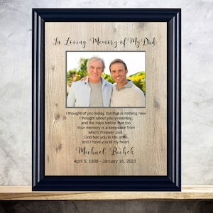 May include: A framed photo memorial with a woodgrain background. The photo shows two men smiling at the camera. The text reads "In Loving Memory of My Dad" and includes a poem about remembering a loved one. The dates "April 5, 1938 - January 16, 2023" are printed below the poem.