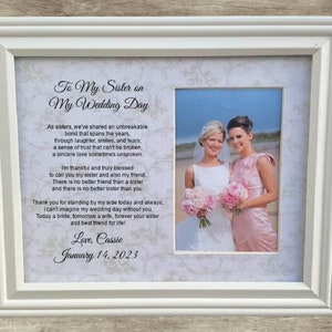 May include: A white picture frame with a photo of two women in wedding attire. The text in the frame reads "To My Sister on My Wedding Day" and includes a poem about the bond between sisters. The date "January 14, 2023" is written at the bottom of the frame.