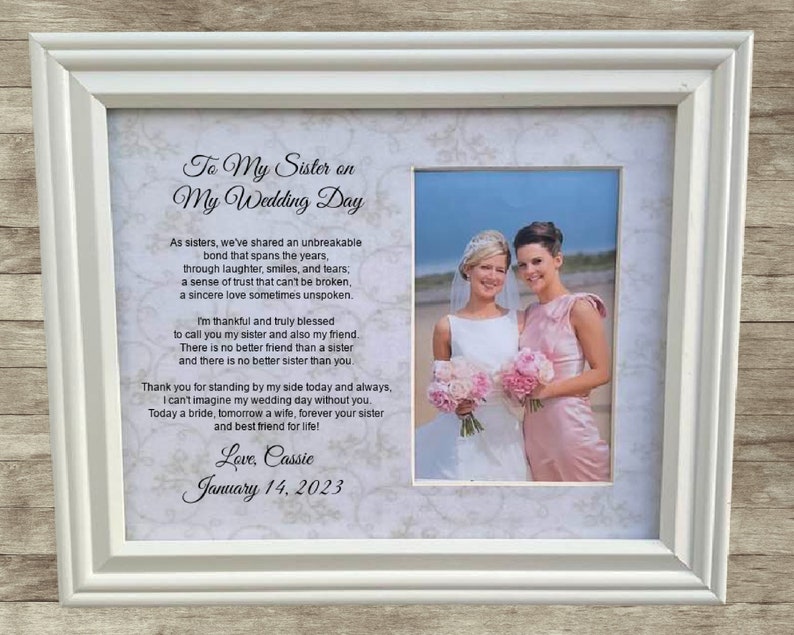 May include: A white picture frame with a photo of two women in wedding attire. The text in the frame reads "To My Sister on My Wedding Day" and includes a poem about the bond between sisters. The date "January 14, 2023" is written at the bottom of the frame.