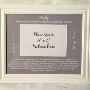 May include: A white picture frame with a gray mat and a message about the adventure of life beginning. The frame has a space for a 6x4 inch photo and the text "Daddy" and "2019".